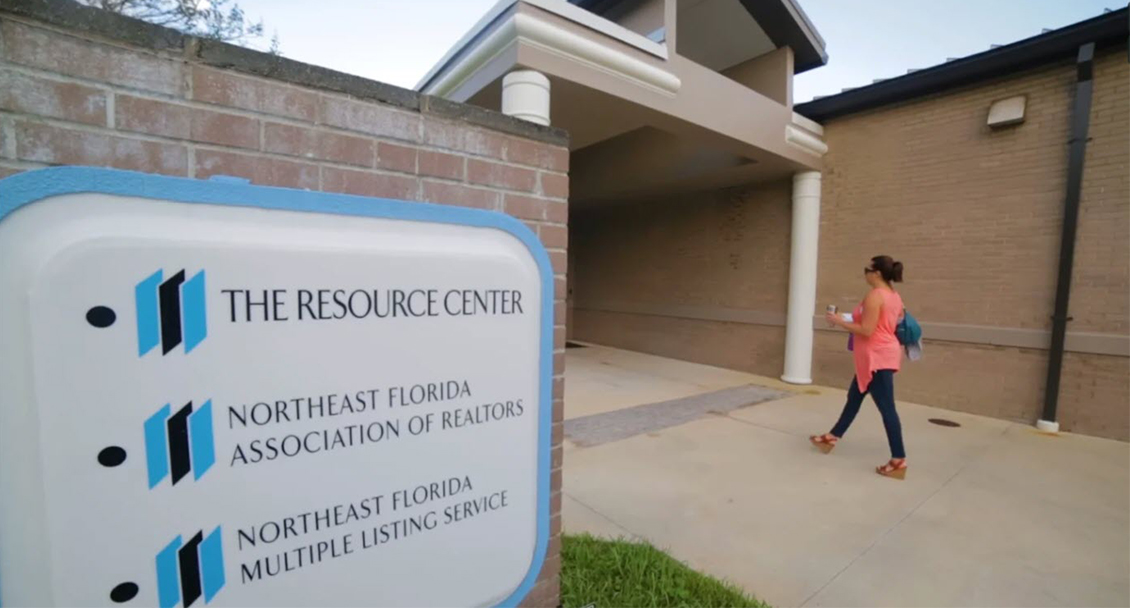 Woman walking into a building with display sign for The Resource Center, The Northeast Florida Association of Realtors and The Northeast Florida Multiple Listing Service
