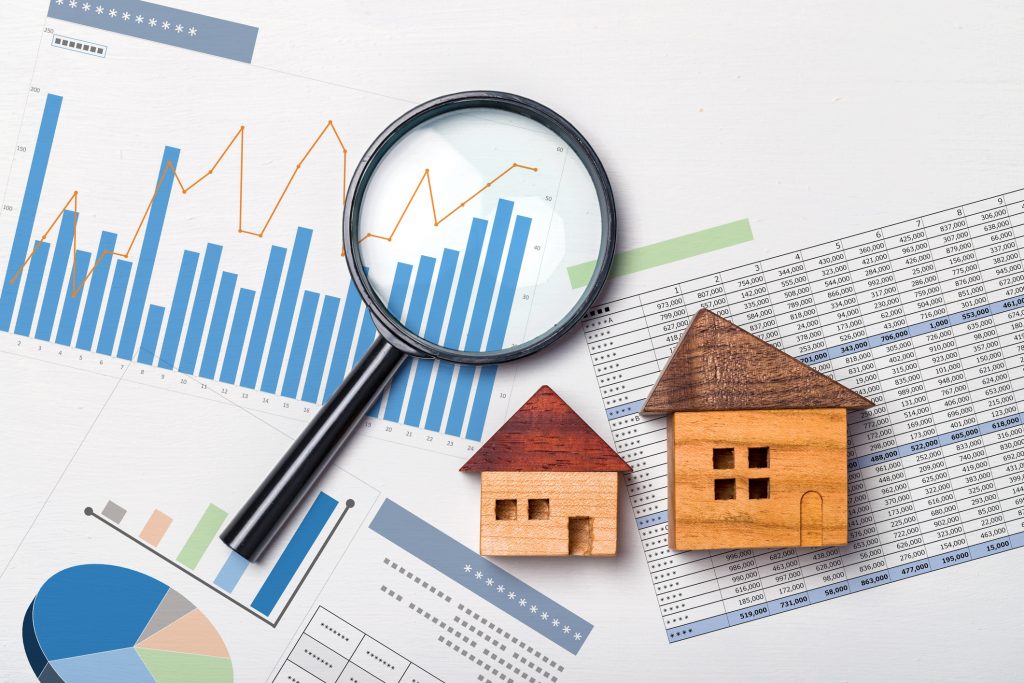 Magnifying glass over charts and images of houses indicating real estate value