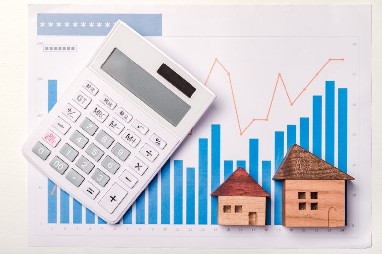 Small Wooden Homes On top of Market Graphs alongside of a Calculator